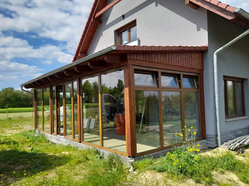 Houten kozijnen en grote glazen schuifdeuren vormen een moderne serre aan een woonhuis.