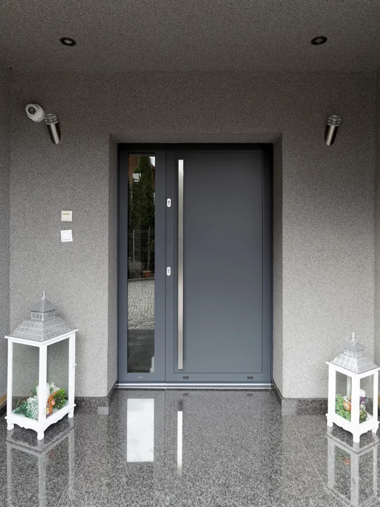 Moderne grijze voordeur met zijlicht, omgeven door een strakke grijze gevel en decoratieve lantaarns op een glanzende granieten vloer.