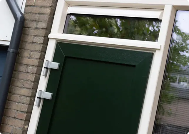 Donkergroene voordeur met bovenlicht en stevige metalen scharnieren aan een bakstenen gevel.